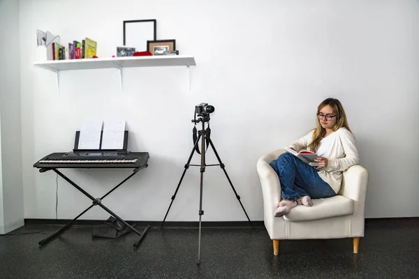 Menina com livro senta-se na cadeira ao lado da câmera fotográfica — Fotografia de Stock