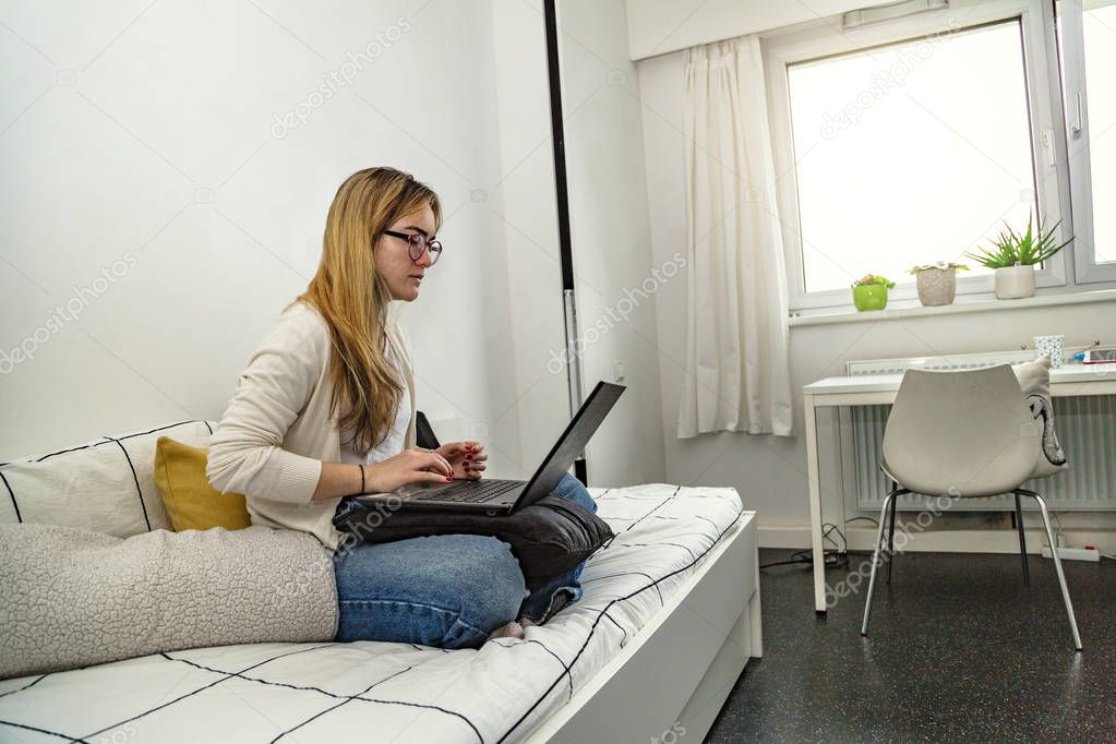 Woman sitting on bed, working on laptop in house