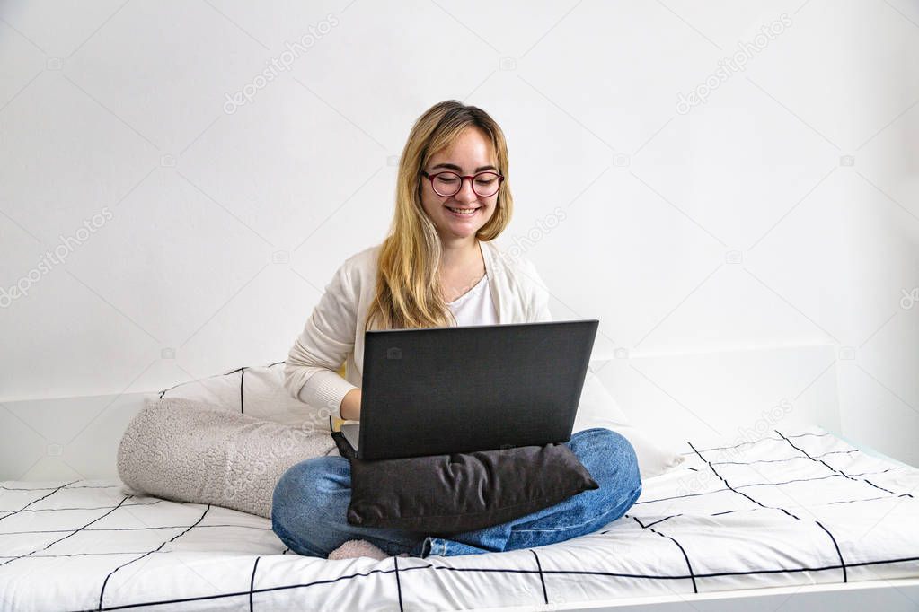 Young girl on bed smiling and working in laptop
