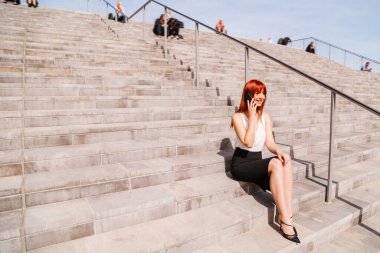 Kız merdivenlerde tek başına oturuyor ve telefonda konuşuyor.