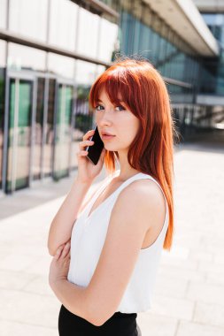 Kızıl saçlı kız telefonda konuşuyor ve kameraya bakıyor.