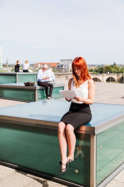 Genç kadın sokakta oturan belgeleri okuyor.