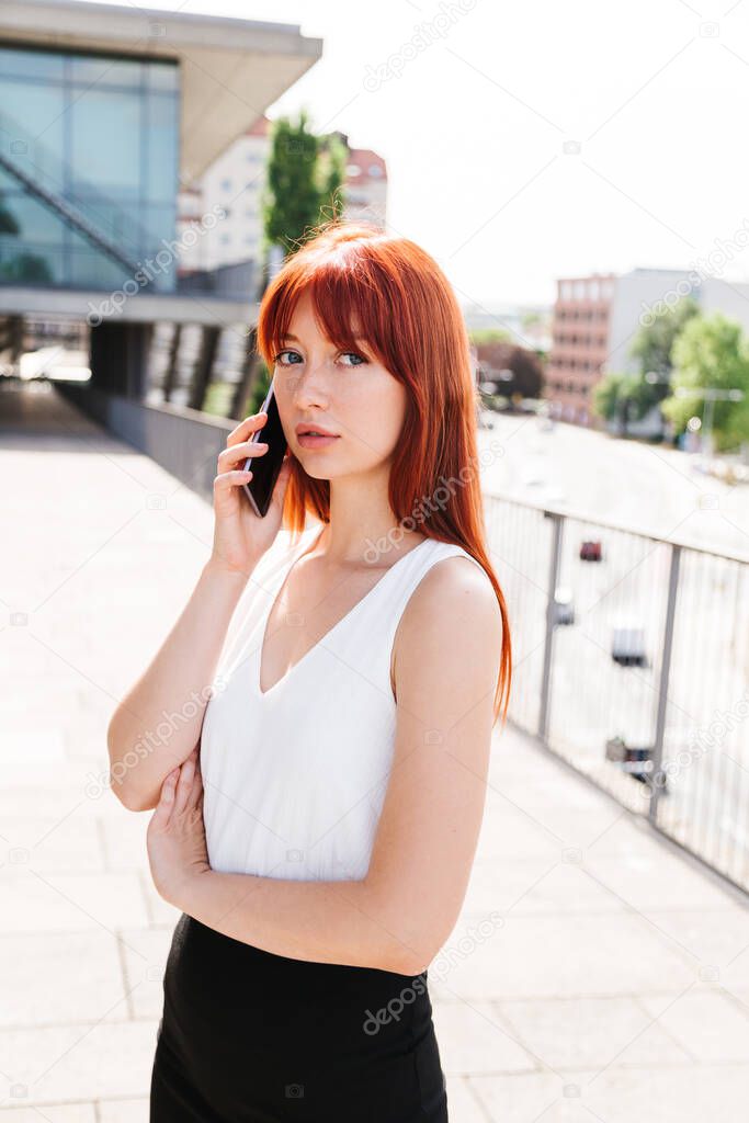 Red-haired girl talks on phone and looks at camera