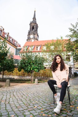 Sokakta tahta arka planda oturan kız.