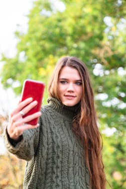 Kazaklı genç kız sonbahar parkında selfie çekiyor.