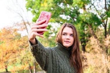 Kazaklı genç kız sonbahar parkında selfie çekiyor.