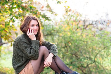 Genç bir kadın parkta cep telefonuyla konuşuyor.