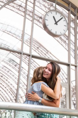 Kız arkadaşlar tren istasyonunda büyük bir saatin altında tanışmışlar ve sarılmışlar.