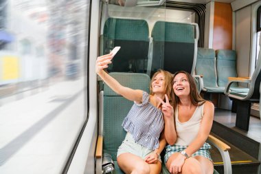 Trende gülümseyen iki kız arkadaş ortak selfie çekiyorlar.