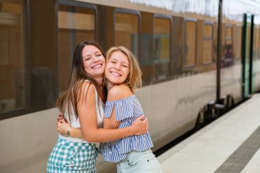 Mutlu genç kadınlar tren istasyonunda duruyorlar.
