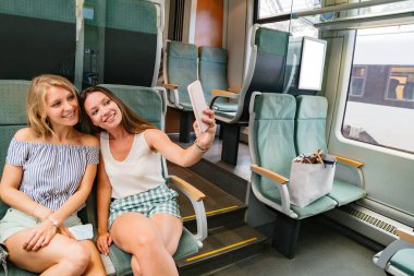 Cep telefonlu iki kız arkadaş selfie çekiyor ve gülümsüyor.