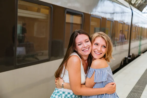 Mutlu genç kadınlar tren istasyonunda duruyorlar.