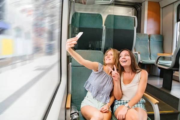 Trende gülümseyen iki kız arkadaş ortak selfie çekiyorlar.