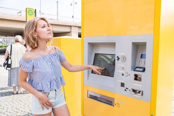 Jovem loira fêmea compra bilhetes em uma máquina de bilhetes na estação de eléctrico — Fotografia de Stock