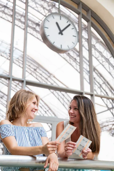 Mulheres bonitas sorrindo com bilhetes em mãos na estação de trem — Fotografia de Stock