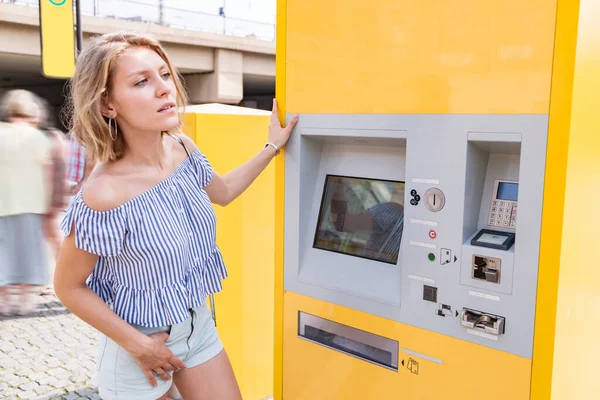 Jovem loira fêmea compra bilhetes em uma máquina de bilhetes na estação de eléctrico — Fotografia de Stock