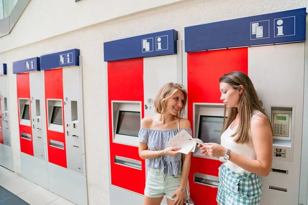 Duas mulheres com bilhetes comprados em uma máquina de venda automática vermelha — Fotografia de Stock