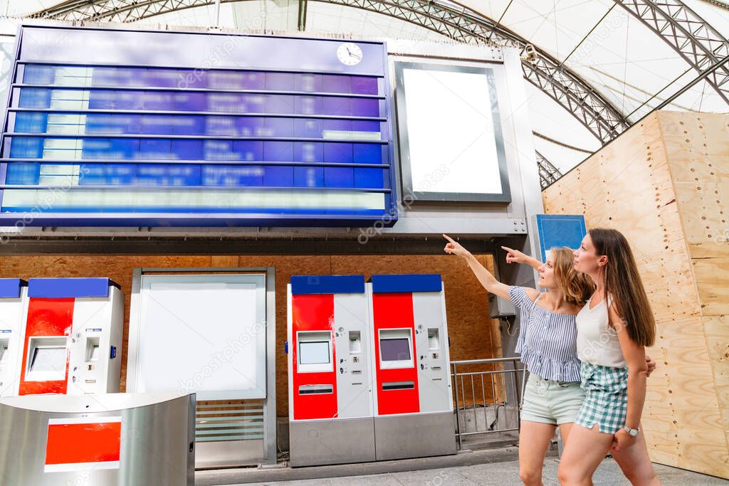 Woman shows her friend schedule on a board at railway station