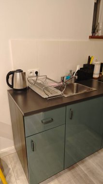 Metal çaydanlık, lavabo ve bulaşık rafı olan küçük bir mutfak köşesi. Çağdaş bir evde kompakt ve işlevsel pişirme alanı kavramı