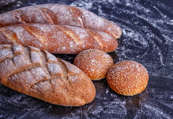 Bäckerei - goldene, rustikale, krustige Brotlaibe und Brötchen auf schwarzem Blech — Stockfoto