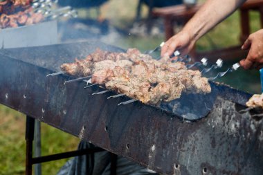 Adam terbiye edilmiş şiş kebap pişiriyor, kuzu eti metal şişte ızgara yapıyor. Beyaz duman, yaklaş. Shish kebabı ızgarada kızartıyordu. Barbekü partisi. Yakın plan..