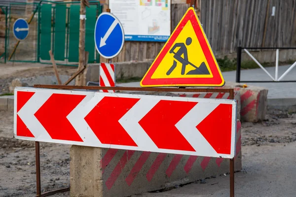 İş devam ediyor. Yol çalışması, yol işaretleri. İş yerindeki erkekler. Şehir caddesinde devam eden bir iş için bazı tabelalar. Bariyerler ve yol işaretleri. İşteki bir işçinin silüeti..