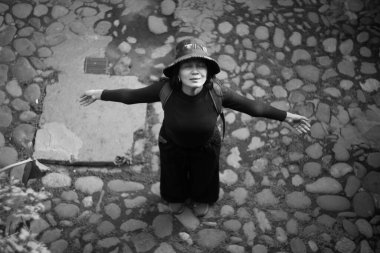 Şapka ve sırt çantası takan kadın turist, kaldırım taşlı bir sokakta kollarını açmış, yeni bir varış noktasını keşfederken özgürlük ve macera hissinin tadını çıkarıyor.