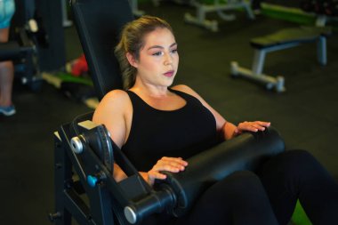 Spor makinesinde bacak presi yapan bir kadın, modern bir sağlık kulübünde dayanıklılık eğitimi ve fitness üzerine odaklanmış, azim, kas bağlılığı ve aktif yaşam tarzı sergiliyor.