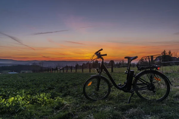 Чорний електричний велосипед із заходом сонця на світло-зеленому лузі навесні увечері — стокове фото