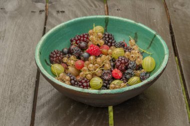 Ahşap kahverengi masa ve turuncu ve yeşil taş tabakta karışık renkli bahçe meyvesi.