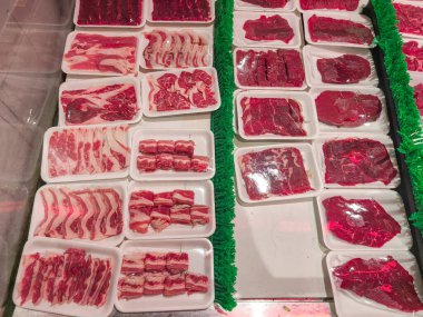 Pazar tezgahında beyaz tepsilerde sergilenen taze kesilmiş et dilimleri ve biftekler, pişirmek ve ızgara yapmak için çeşitli kırmızı et kesimleri sergileniyor..