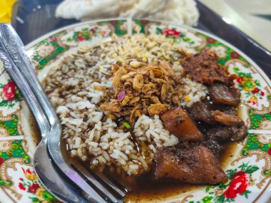 Geleneksel Endonezya usulü pirinçli biftek çorbası, çiçek desenli bir kasede servis edilir, üstü kızarmış soğan ve sambal ile kaplanır, yanında da çıtır krakerler..