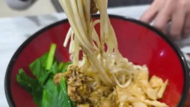 Lezzetli bir kase Mie Ayam, klasik Endonezya usulü tavuk çorbası. Bir insan erişteyle sosları karıştırmak için çubuk kullanır. Tavuk, sebze ve gevrek mantı da dahil..