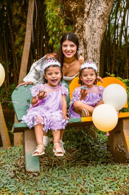 Smiling mother and twin daughters pose with cupcakes during joyful birthday in nature