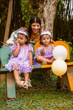 Mother and twin daughters share joyful moment with cupcakes during birthday outdoors