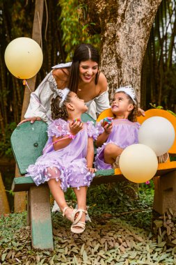 Twin daughters smile at mother during joyful birthday moment with cupcakes outdoors