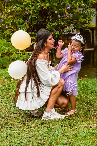 Daughter wipes her face, laughing after a loving kiss from her mother during an outdoor birthday party