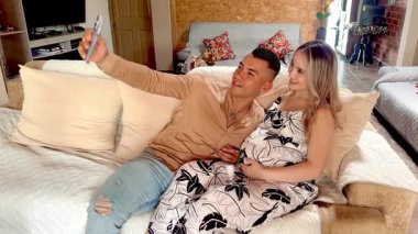 Colombian couple takes joyful selfie on sofa, laughs together while reviewing photos in rural home