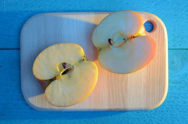 Apple cuted in half on a wooden board on turquoise table with a long blue shadow — Stock Photo, Image