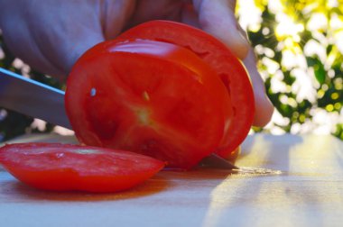 bir kesme tahtası ağaçlar ve günbatımı akşam arka planı üzerinde bir domates bir el ve bıçak ile dilimleme portre