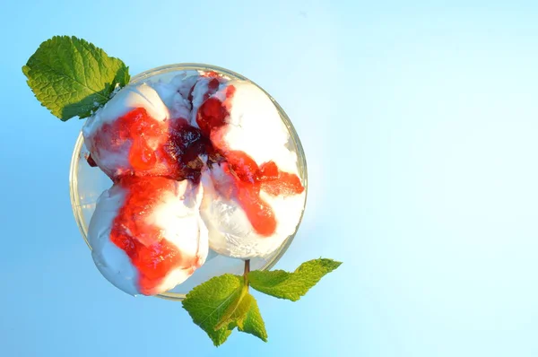 top view of white ice cream with red jam and mint leaf on a blue background