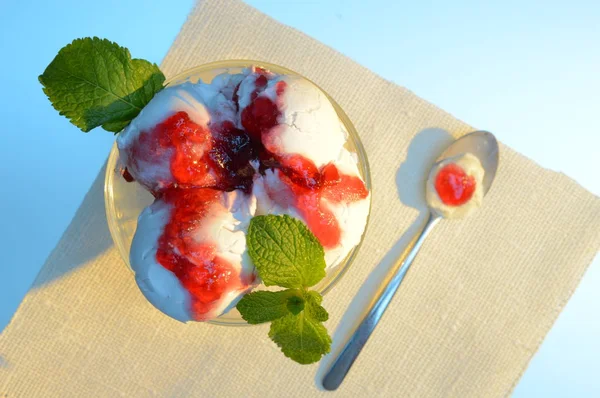 dessert spoon with white ice cream and red jam lies near the plate with ice
