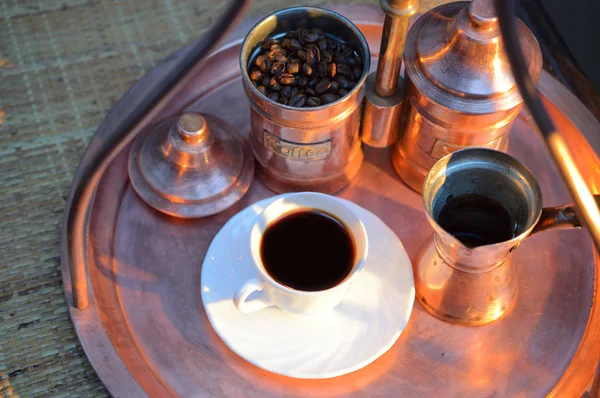 a Cup of coffee near the sugar bowl and a container with coffee on a copper tray and a rattan table