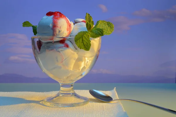 white ice cream with jam and mint leaves in a vase against the background of mountains and cloudy sky