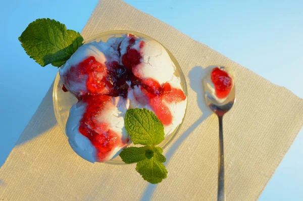 dessert spoon with white ice cream and red jam lies near the plate with ice cream