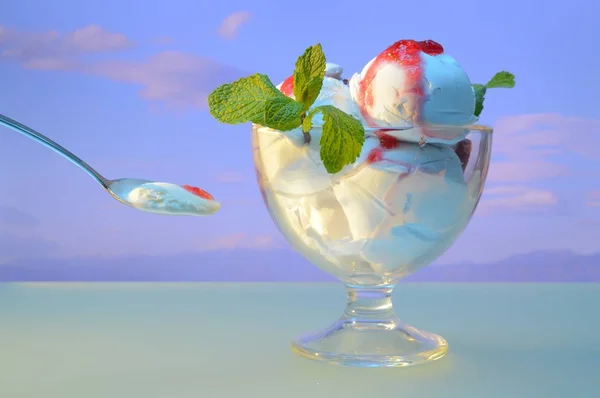 white ice cream with jam and mint leaves in a vase against the background of mountains and cloudy sky