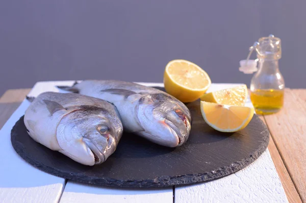 Dorado fish on a black plate with lemon — стоковое фото
