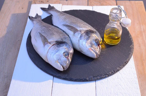 Dorado fish on a black plate with olive oil bottle — стоковое фото
