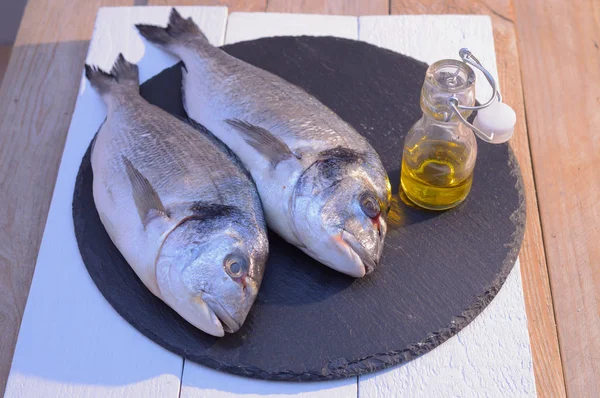 Dorado fish on a black plate with olive oil bottle — стоковое фото