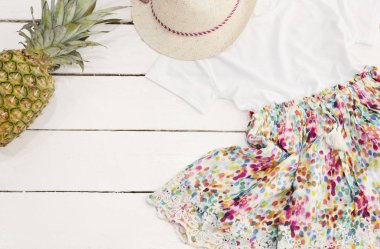 Hasır şapka, çiçek elbise, ananas. Beyaz eski ahşap arka plan.